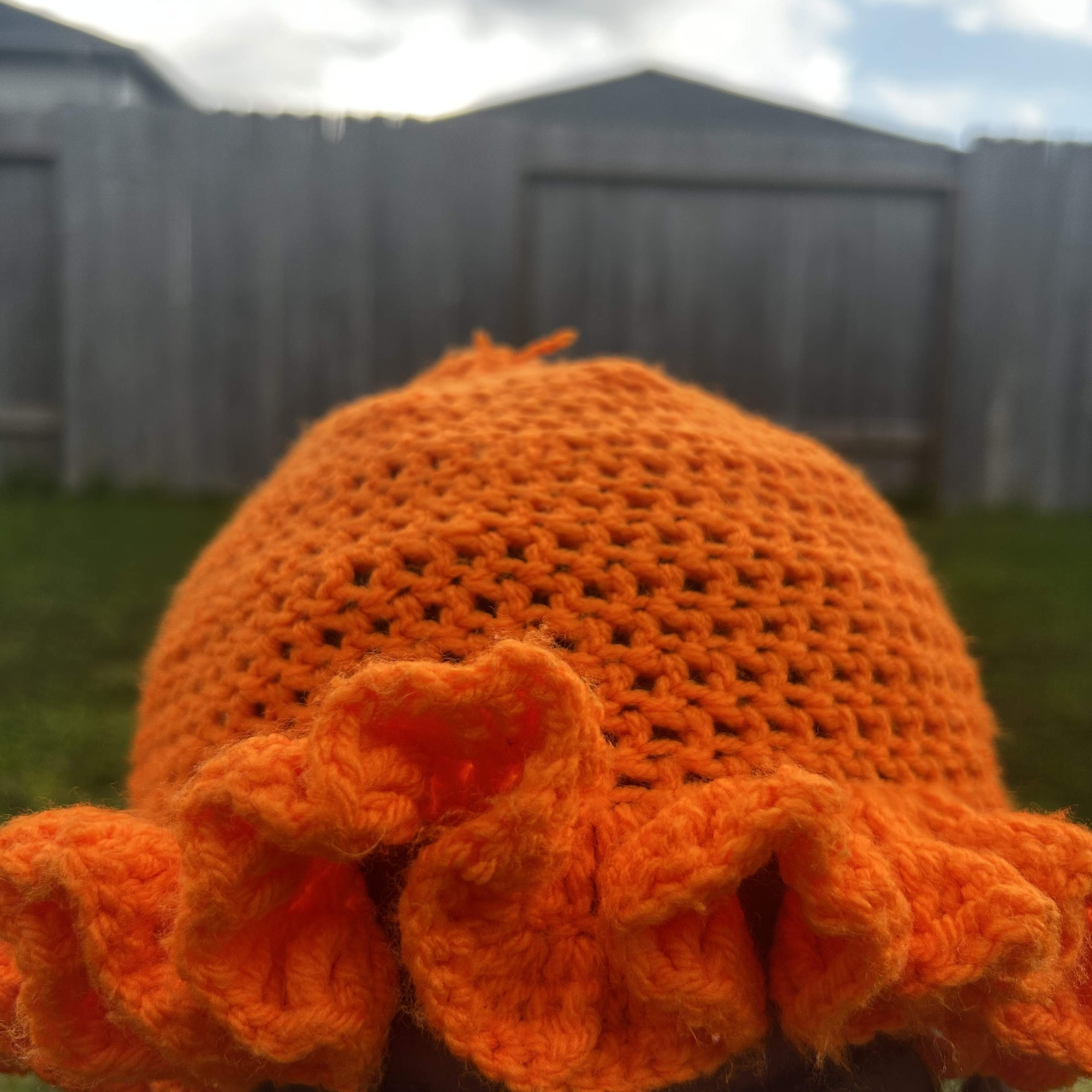 Front detail of handmade Jamaican bright orange crochet hat with curled monochrome ruffle brim