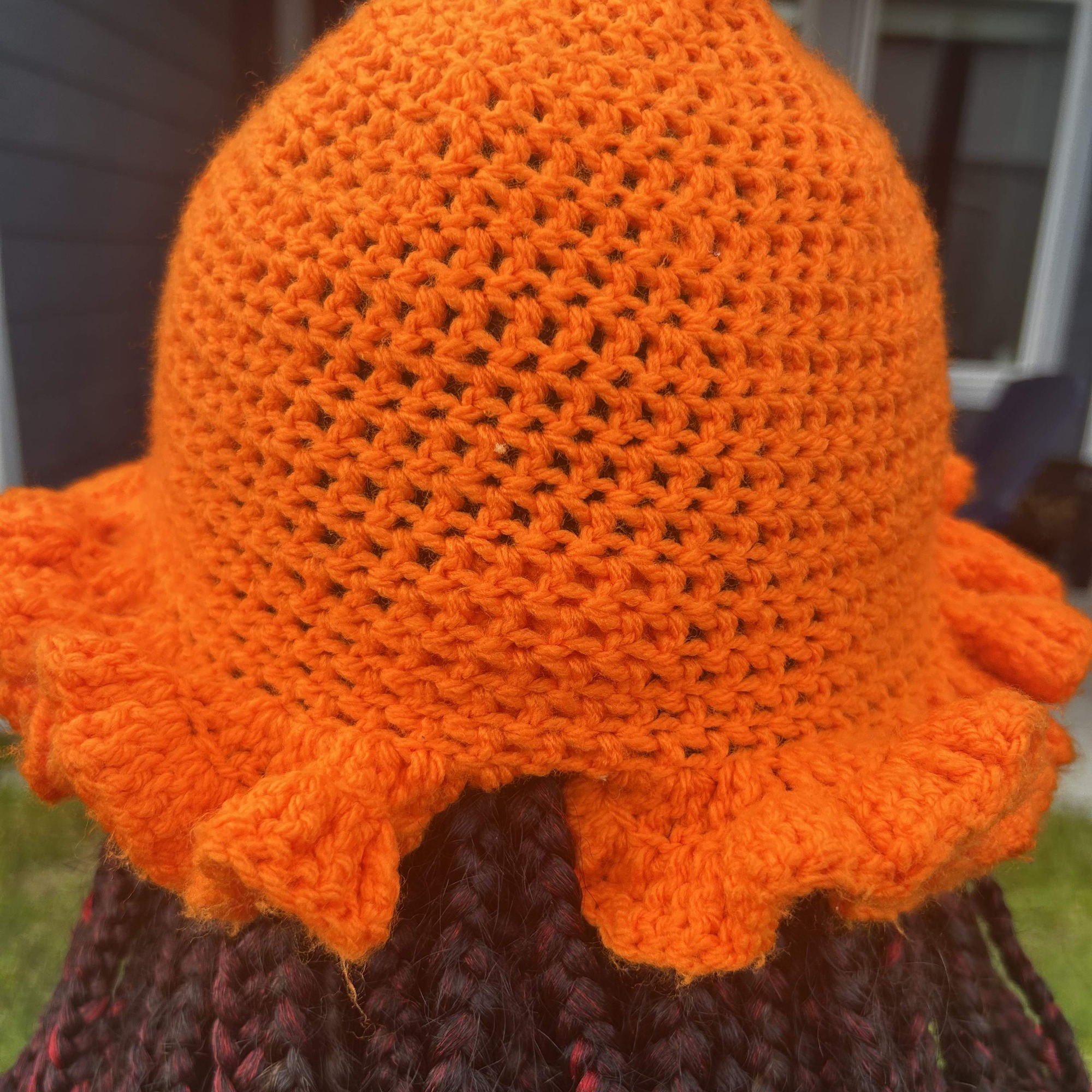 Rear view of handmade Jamaican bright orange crochet hat with open stitch crown and sculptural ruffled brim