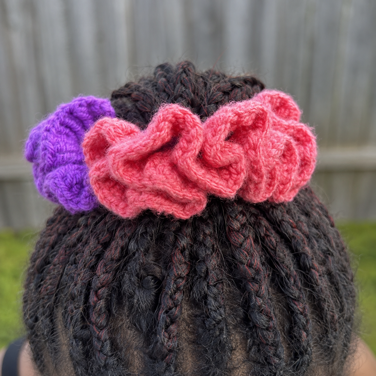 Handmade Jamaican coral-pink and deep-purple colorblock crochet scrunchie shown worn in braided hair
