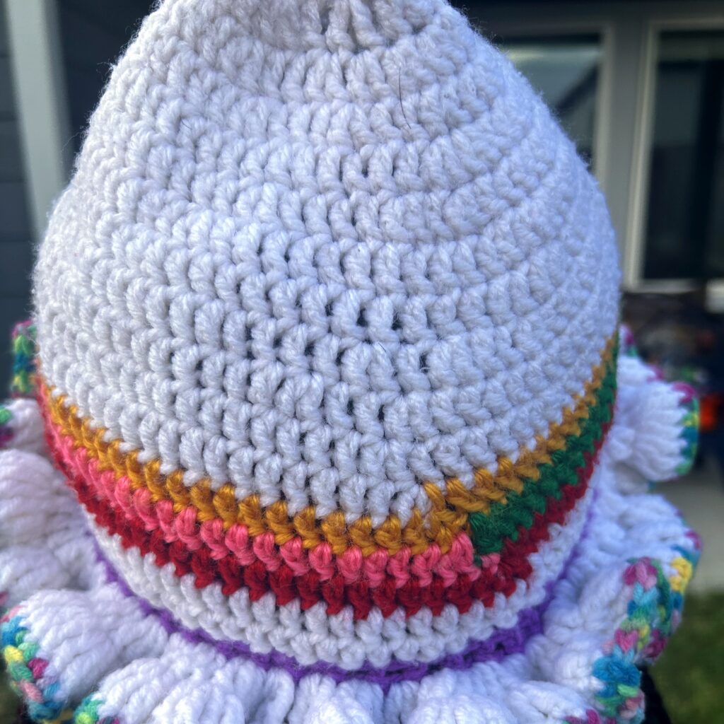 Close-up of handmade Jamaican cream crochet hat with gold, green, red, pink and purple bands and multicolor ruffle brim