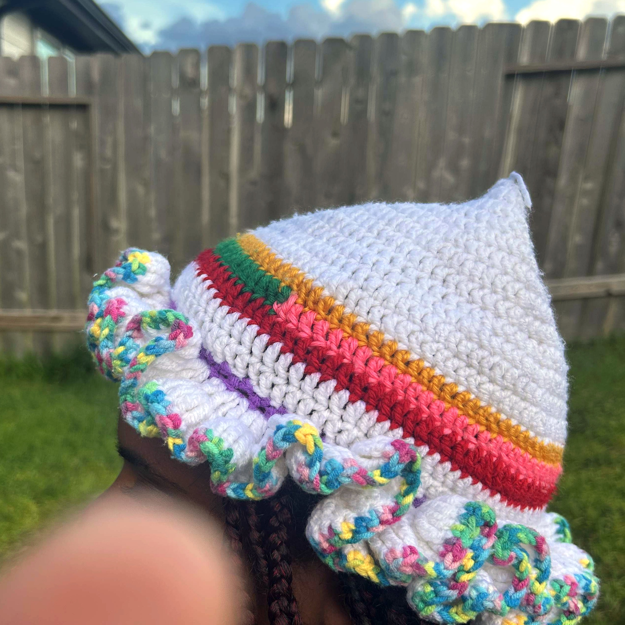Side profile of handmade Jamaican cream crochet hat with pointed crown, colorful striped bands and multicolor ruffle brim