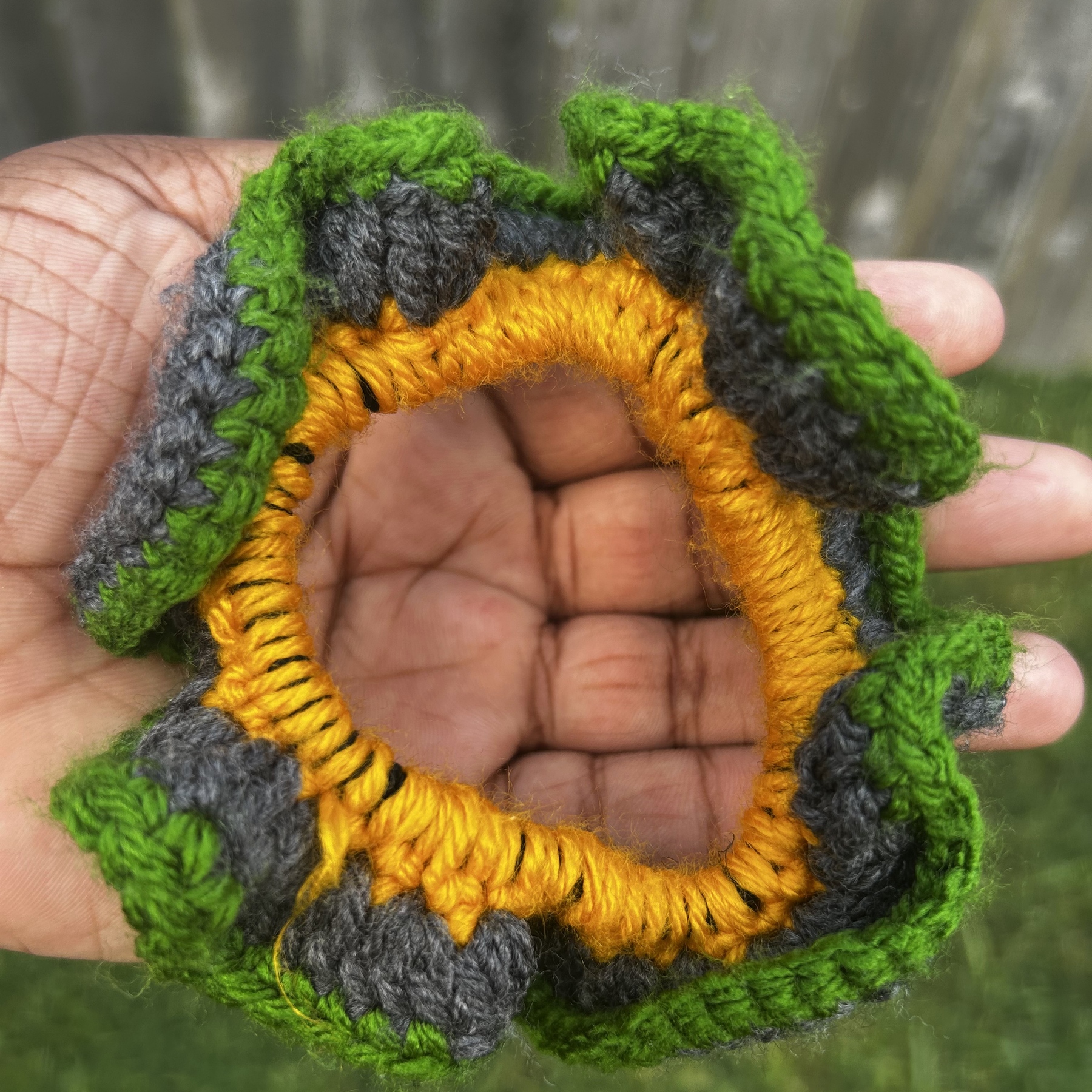 Close detail of handmade Jamaican green, charcoal-gray and golden-yellow crochet scrunchie