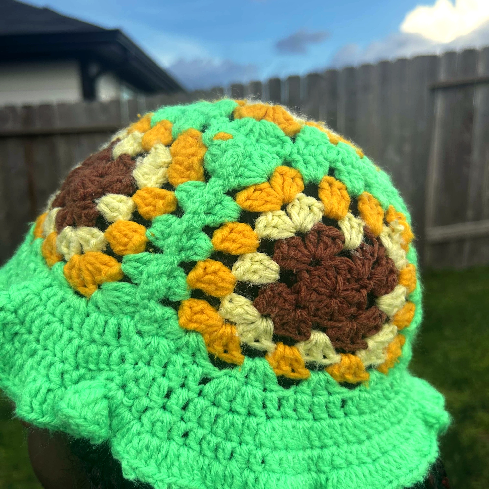 Angled view of handmade Jamaican green crochet bucket hat with brown cream and gold granny-stitch motifs
