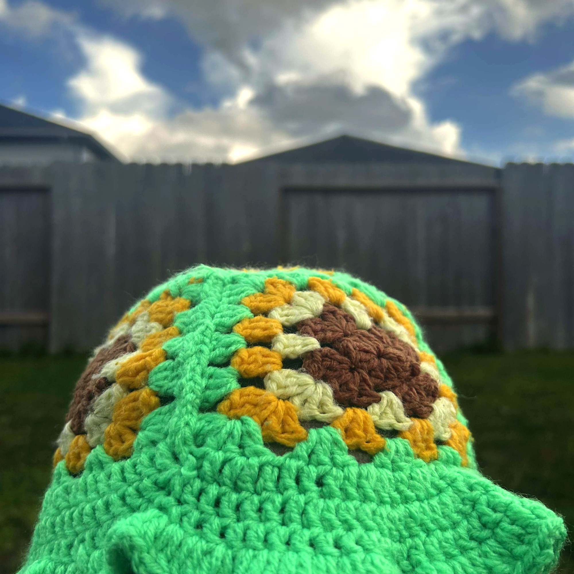Front view of handmade Jamaican green granny-stitch crochet bucket hat with floral crown and flared brim