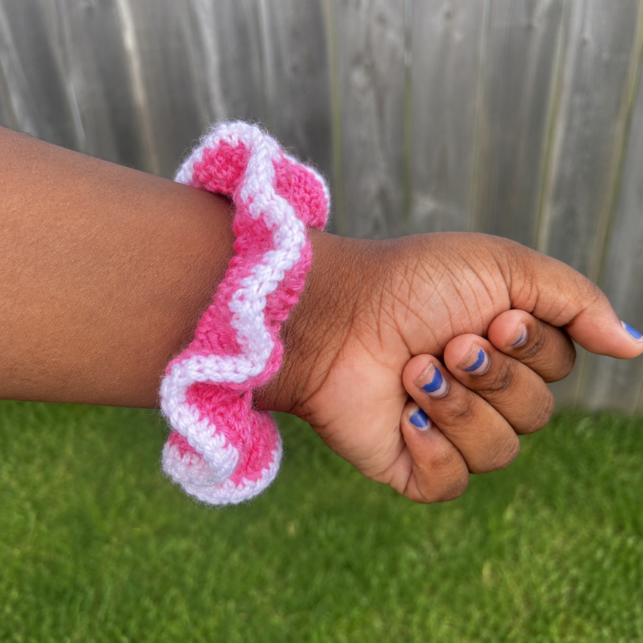 Handmade Jamaican hot-pink and white crochet scrunchie shown on wrist