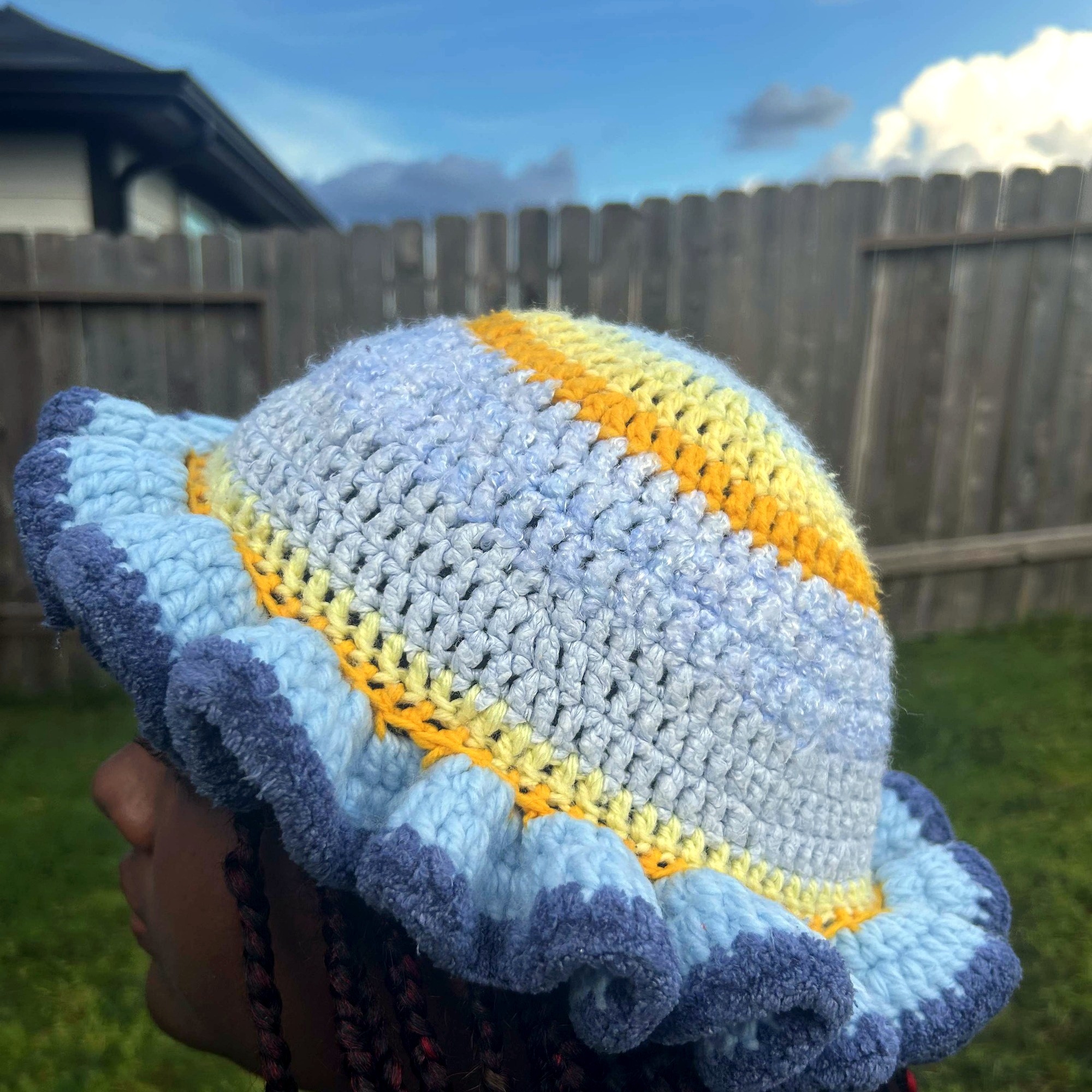 Angled view of handmade Jamaican light blue and gold crochet hat with deep-blue ruffle brim