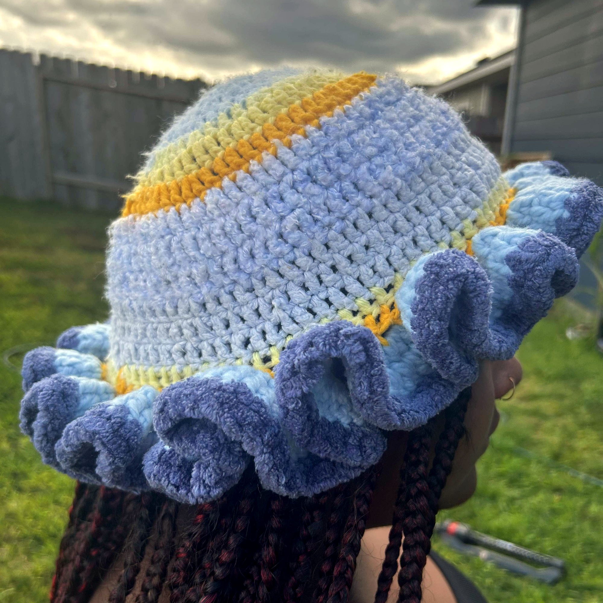 Side profile of handmade Jamaican light blue and gold crochet hat with layered deep-blue ruffle brim