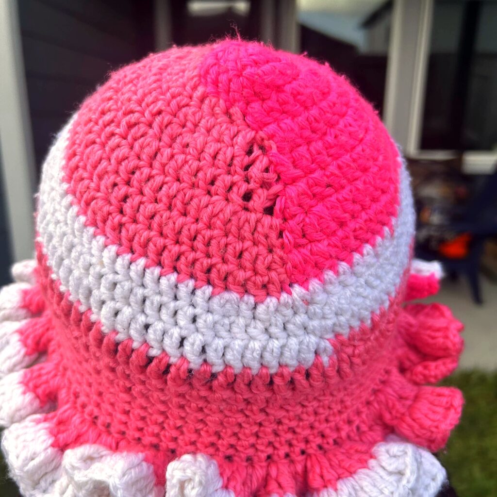 Close angled view of handmade Jamaican pink and white crochet hat with full white ruffle brim