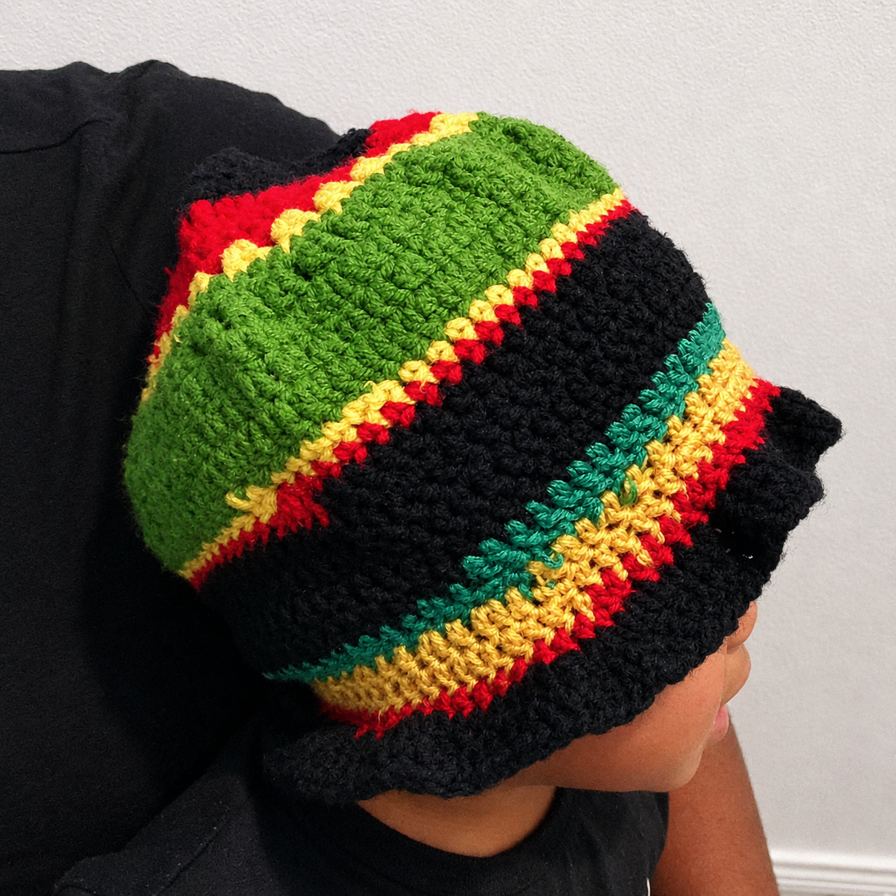 Side worn view of handmade Jamaican red gold green and black crochet bucket hat