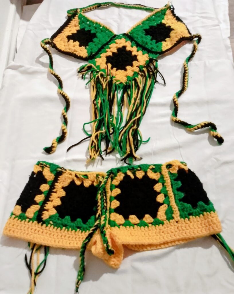 Handmade green, gold and black Jamaican crochet clothing set arranged flat with fringe details